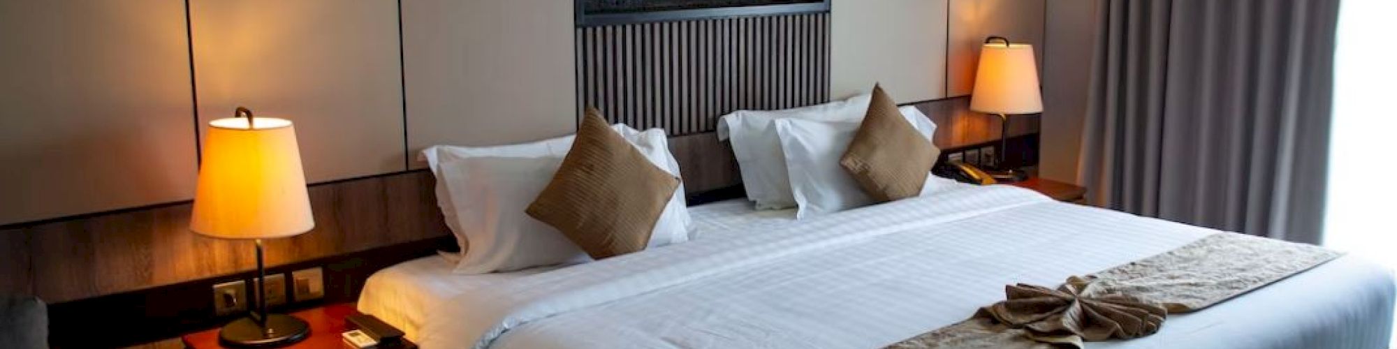 A cozy hotel room with a large bed, elegant decor, two bedside lamps, and soft lighting, creating a welcoming atmosphere.
