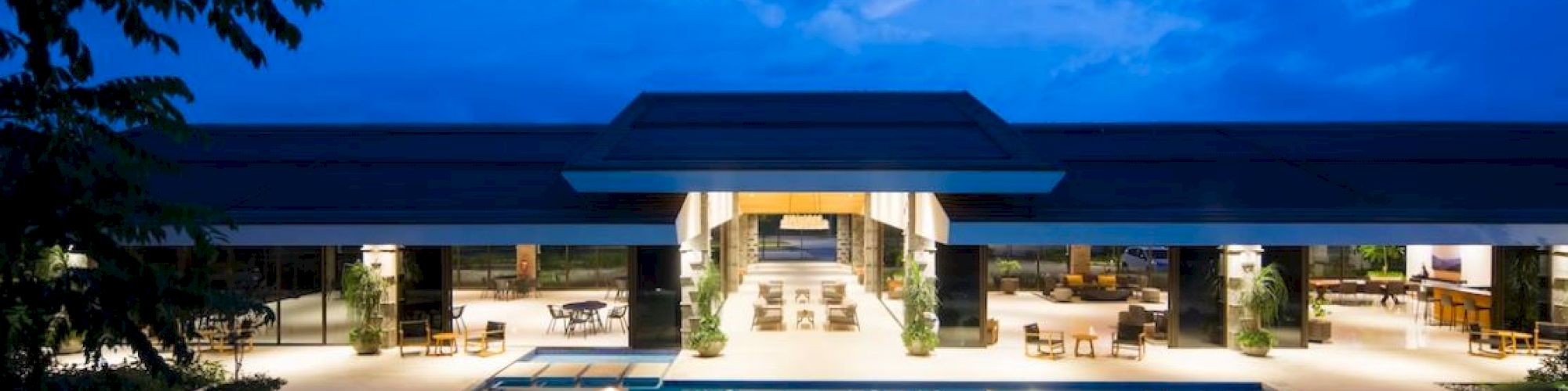 A luxurious poolside view at night with a modern building, outdoor seating, and a clear sky reflecting in the water.