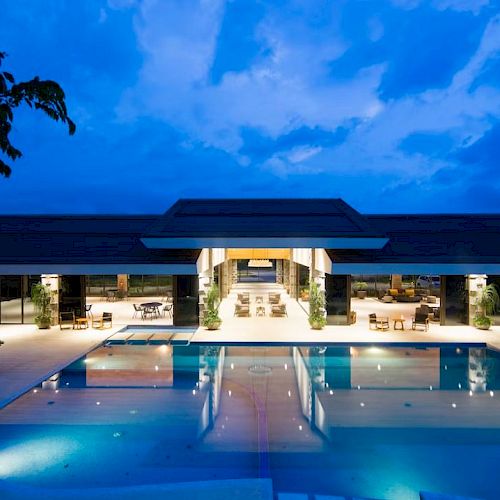 A luxurious building with a central open area and a large illuminated pool reflecting the evening sky, creating a serene ambiance.