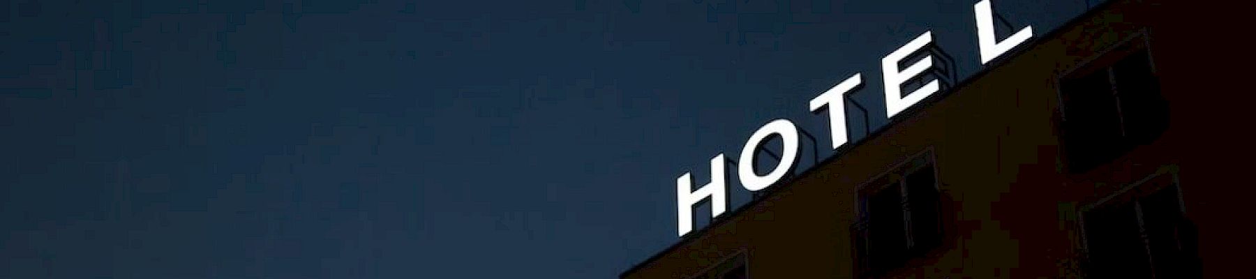 A building with a bright "HOTEL" sign on top, set against a dark, evening sky, with windows visible on the side wall.