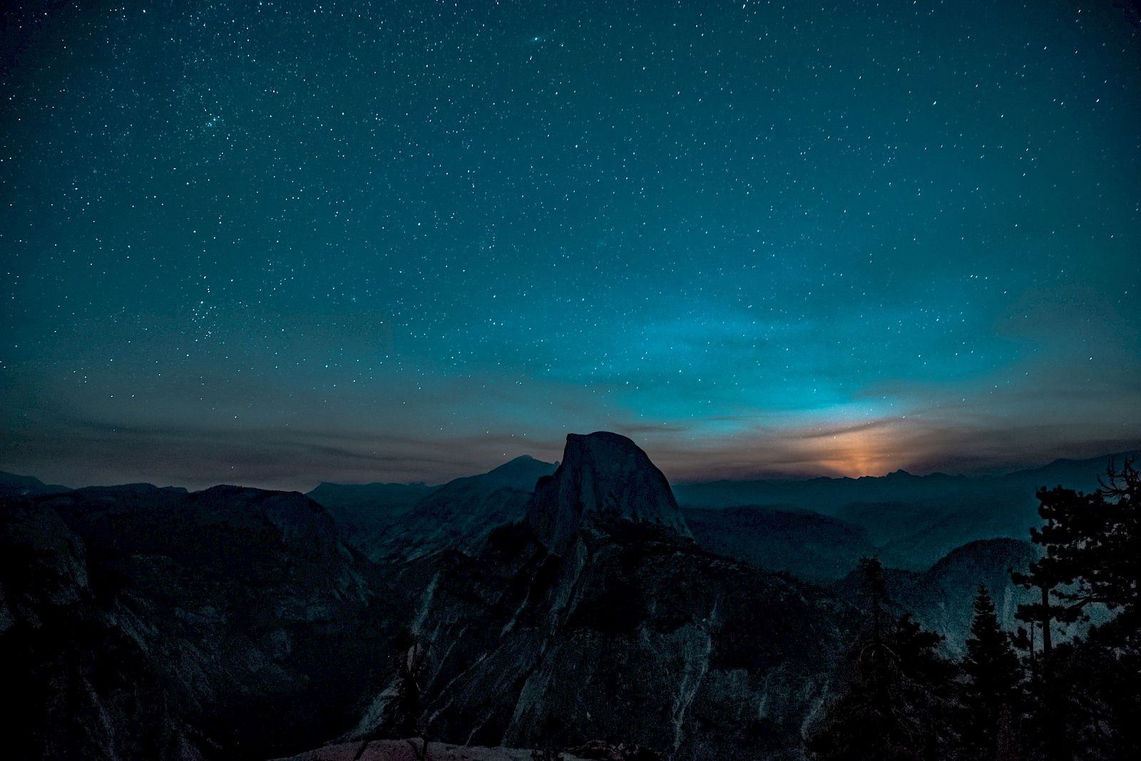 A starry night sky over a mountainous landscape, with a glowing horizon.