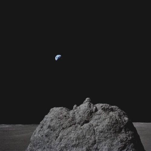 A rocky lunar surface with Earth visible in the distant black sky, creating a striking space scene.