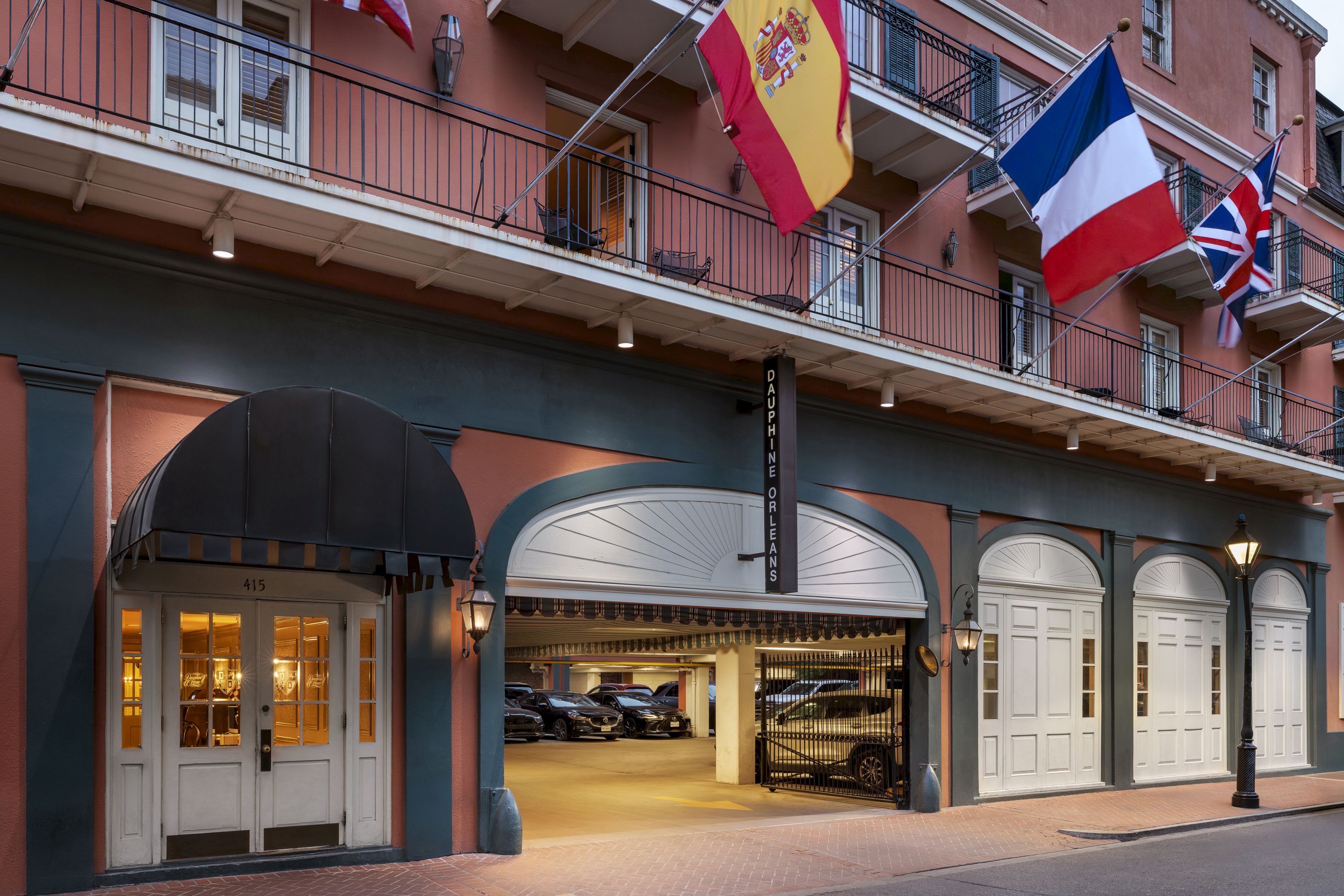 The exterior of a hotel with a balcony, flags, and a garage entrance.