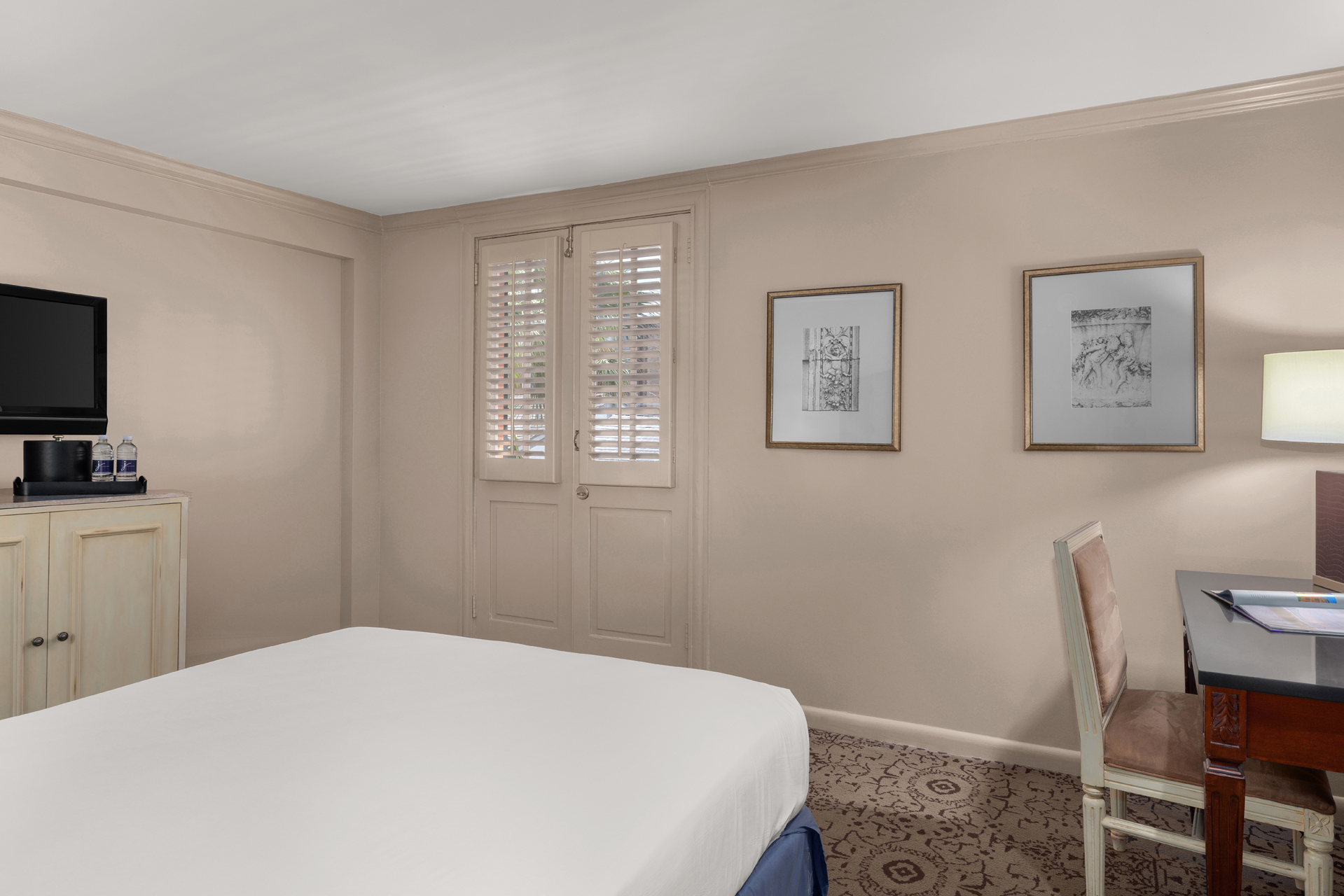 A hotel room with a bed, desk, chair, and TV.