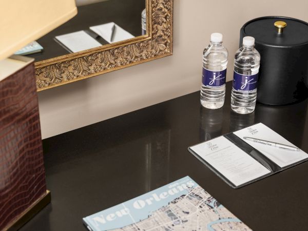 Desk with a detailed mirror, two water bottles, a black ice bucket, hotel stationery, a pen, and a New Orleans map.