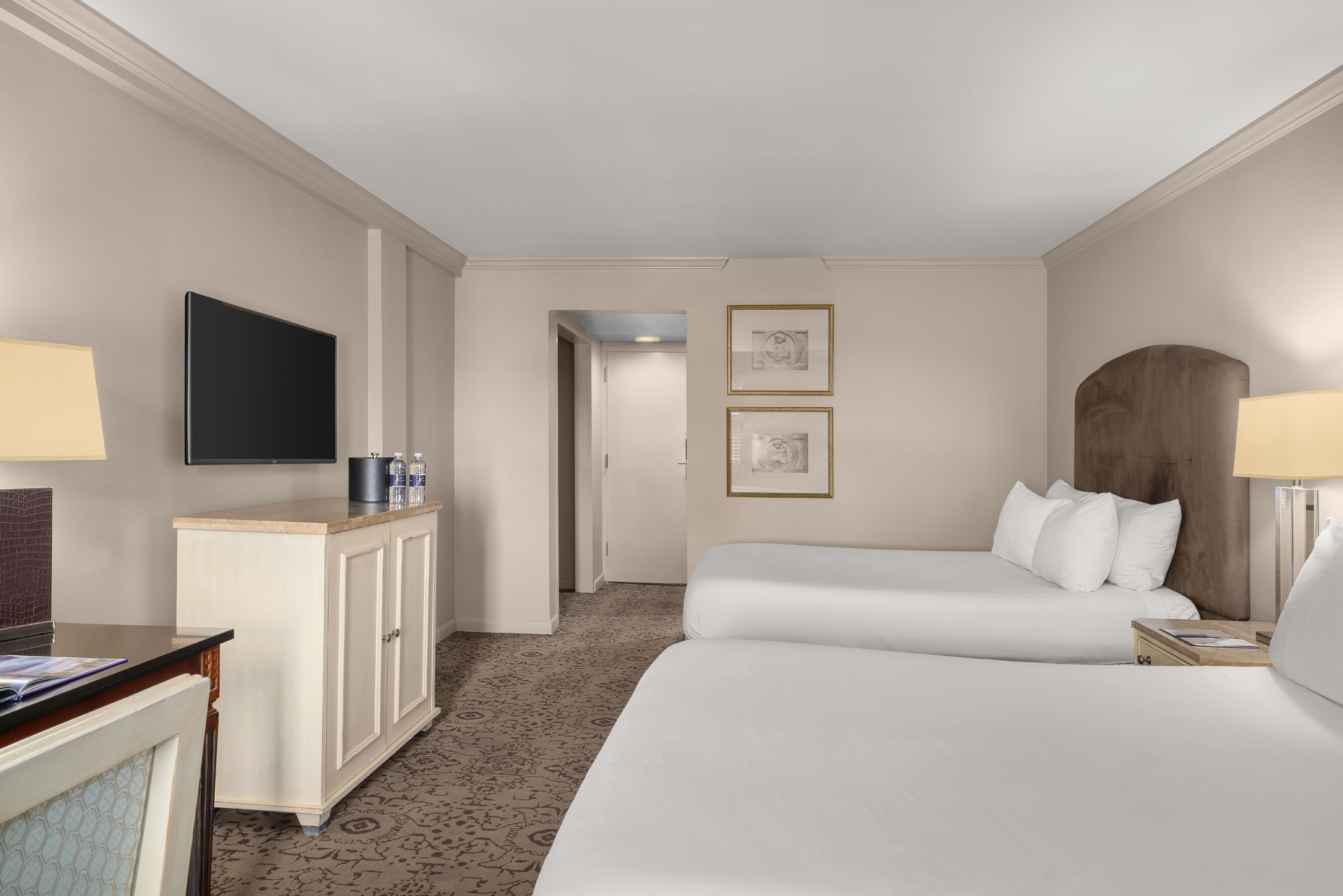 A hotel room with two beds, a TV, and a dresser.