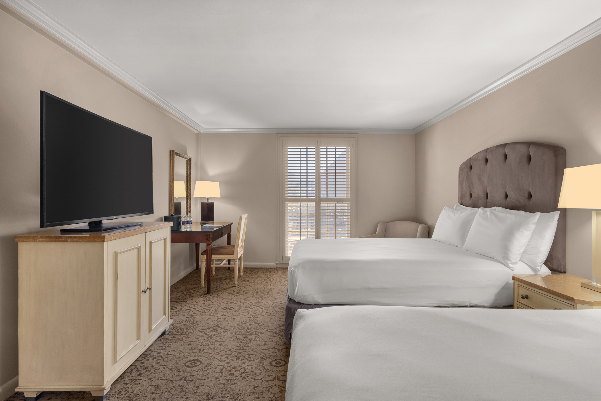 A hotel room with two beds, a TV, and a desk.