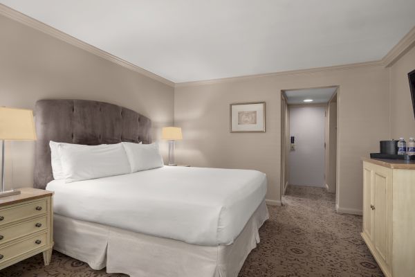 A neatly arranged hotel room with a large bed, nightstands, artwork on the wall, and a dresser with water bottles.