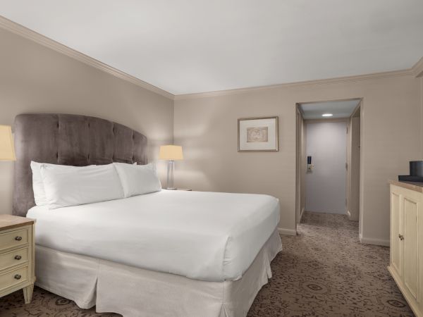 A neatly arranged hotel room with a large bed, nightstands, artwork on the wall, and a dresser with water bottles.