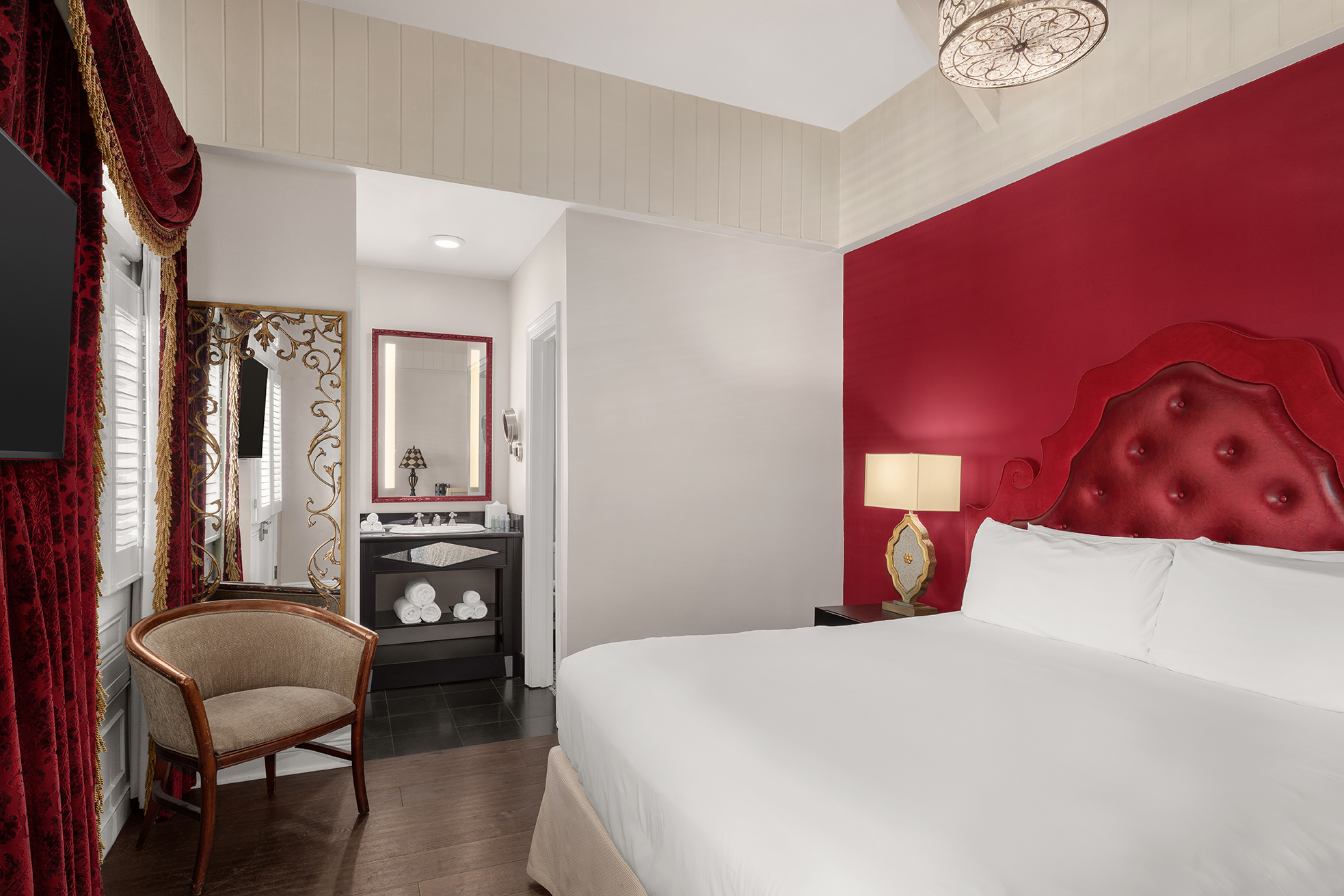 A hotel room with a red accent wall, a white bed, and a chair.