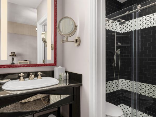 A bathroom with a sink, mirror, and shower. The area features dark tiles and decorative patterns, with essentials neatly arranged on the counter.