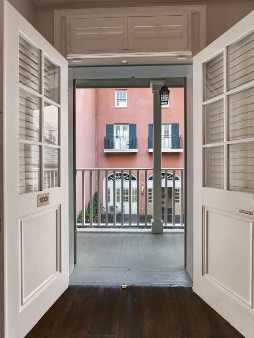 Looking through open double doors at a balcony railing, with a building visible across a courtyard.