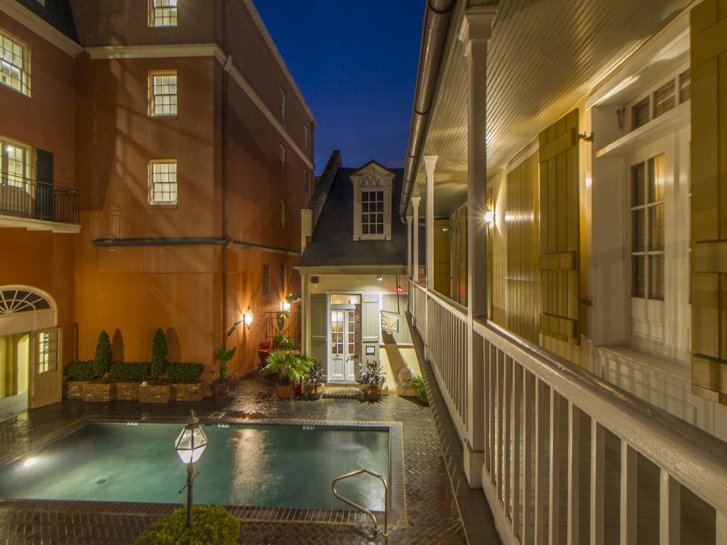 A nighttime view of a hotel pool area surrounded by buildings with balconies and plants.