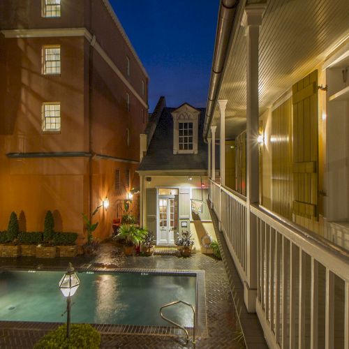 The image shows a small courtyard with a pool, surrounded by buildings, lit warmly at night.