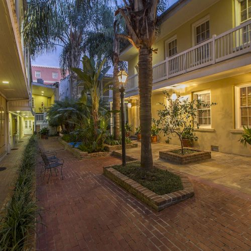 A charming courtyard with brick pathways, potted plants, outdoor lights, and a two-story building with balconies and windows.