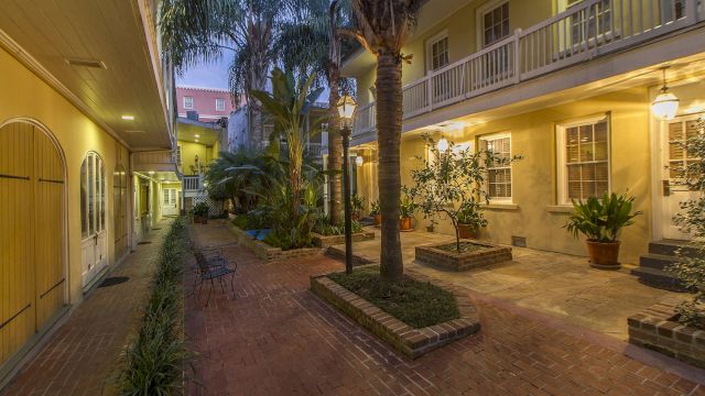 A serene courtyard with a brick pavement, palm trees, and a balcony.