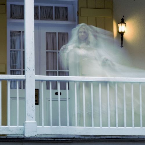 A semi-transparent figure in a flowing garment appears ghostly on a porch.