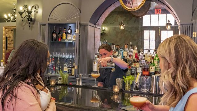 Two women at a bar with a bartender serving drinks.