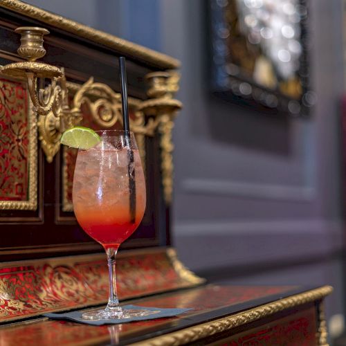 A cocktail with a lime slice and straw, set on an ornate, decorative surface in an elegant, dimly-lit room.
