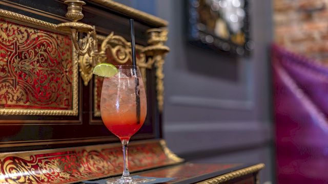 A cocktail with a lime wedge and straw on a bar