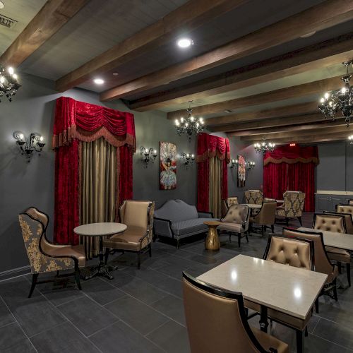 The image shows an elegant room with vintage decor, red curtains, chandeliers, paintings, plush chairs, and tables on a dark tiled floor.