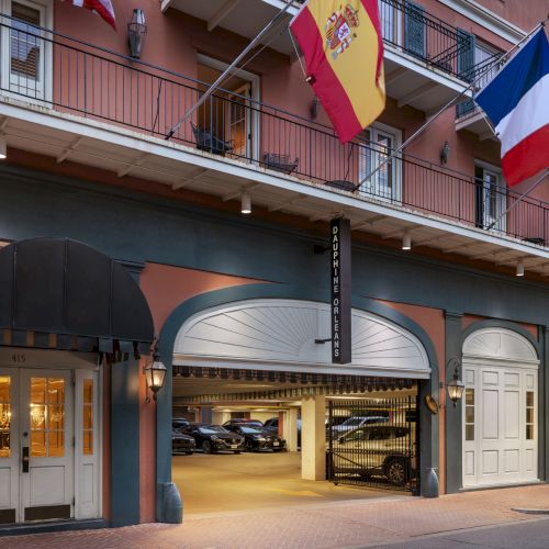 A building with flags of Spain, France, and the UK; features an open garage with parked cars and a black awning over the entrance.