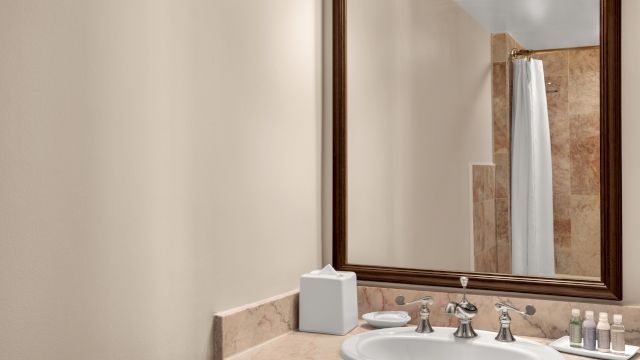 A bathroom sink with a large mirror, marble countertop, and silver faucet.
