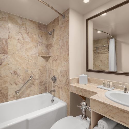 A bathroom with a tiled bathtub, shower, sink, and mirror. There are toiletries and towels neatly arranged on the countertop.