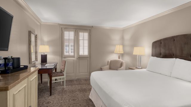 A hotel room with a large bed, desk, chair, and television.