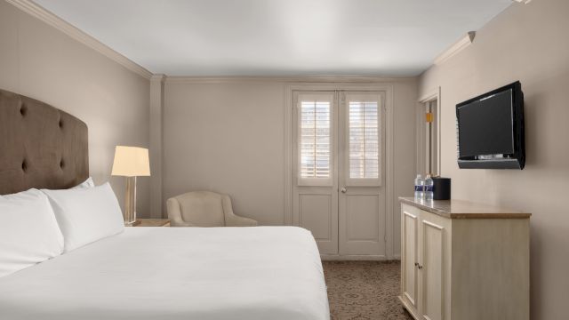 A wide view of a hotel room with a bed, TV, lamp, chair, and door.