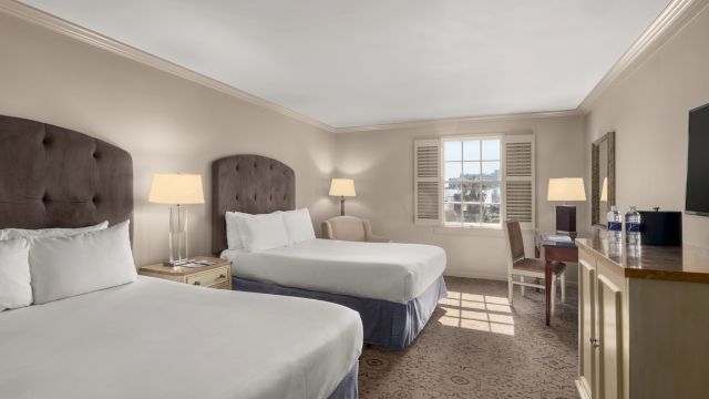 A hotel room with two twin beds, a desk, and a window.