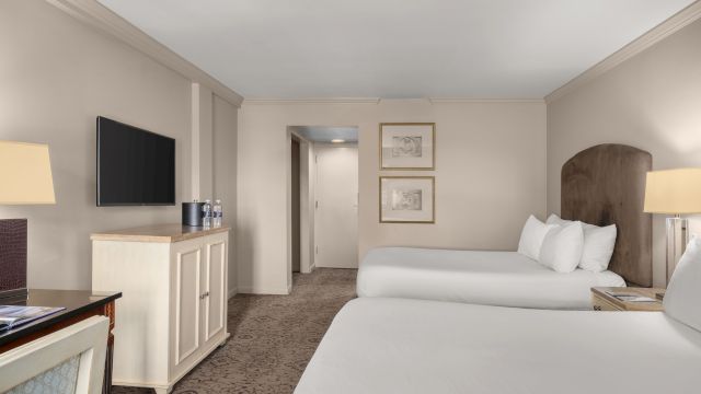 A wide view of a hotel room with two beds, a TV, and a desk.