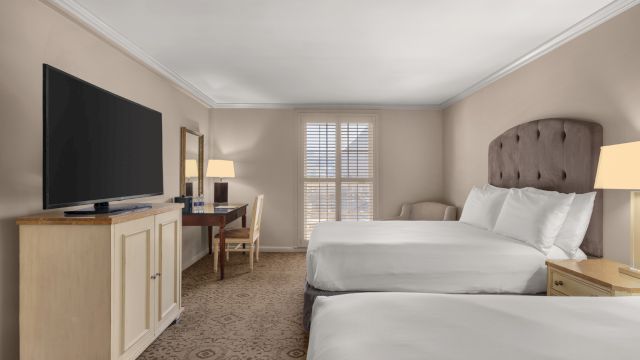 A hotel room with two beds, a desk, and a TV.