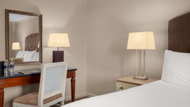 A hotel room with a bed, desk, chair, and mirror.