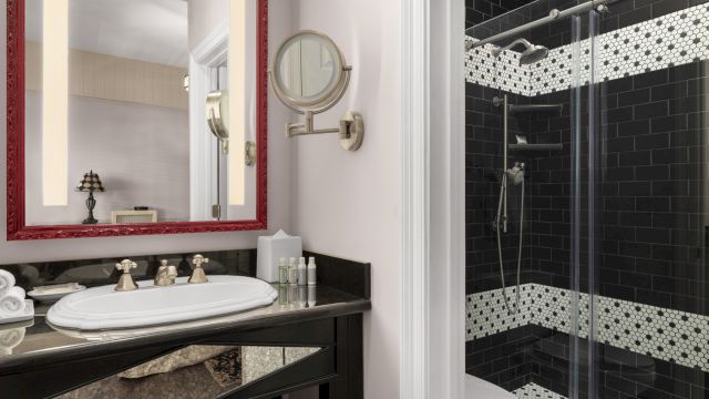 A bathroom with a black and white tiled shower, a sink with a red-framed mirror above it, and a glass door.