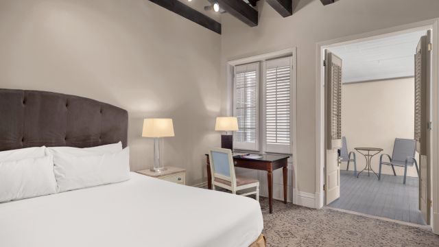 A hotel room with a bed, desk, nightstand, and doorway leading to a small balcony area.