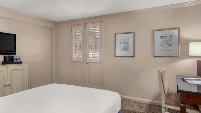 A wide view of a hotel room with a bed, desk, TV, and artwork on the walls.