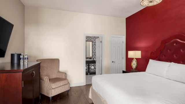 A wide view of a hotel room with a bed, chair, TV, and doorway.