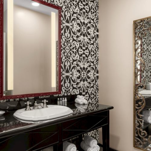 A bathroom with ornate black and white wallpaper, a mirror, a sink, and decorative elements on the counter and walls.