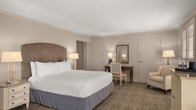 A wide view of a hotel room with a bed, desk, chair, and nightstand.