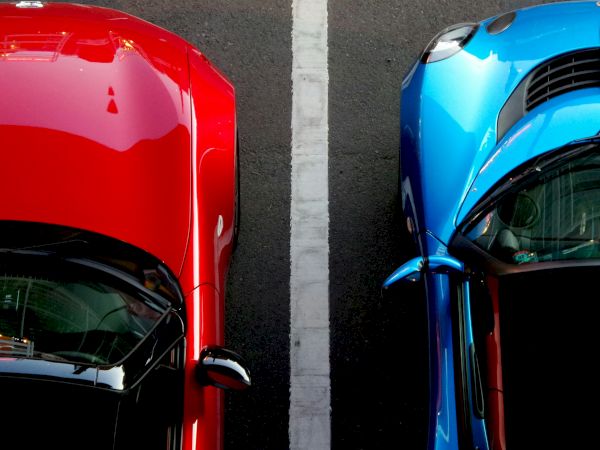 Top-down view of a red car and a blue car parked side by side, separated by a white line.