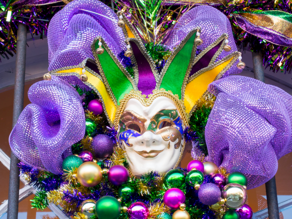 A colorful Mardi Gras-style mask with purple feathers, green and gold accents, and festive beads.