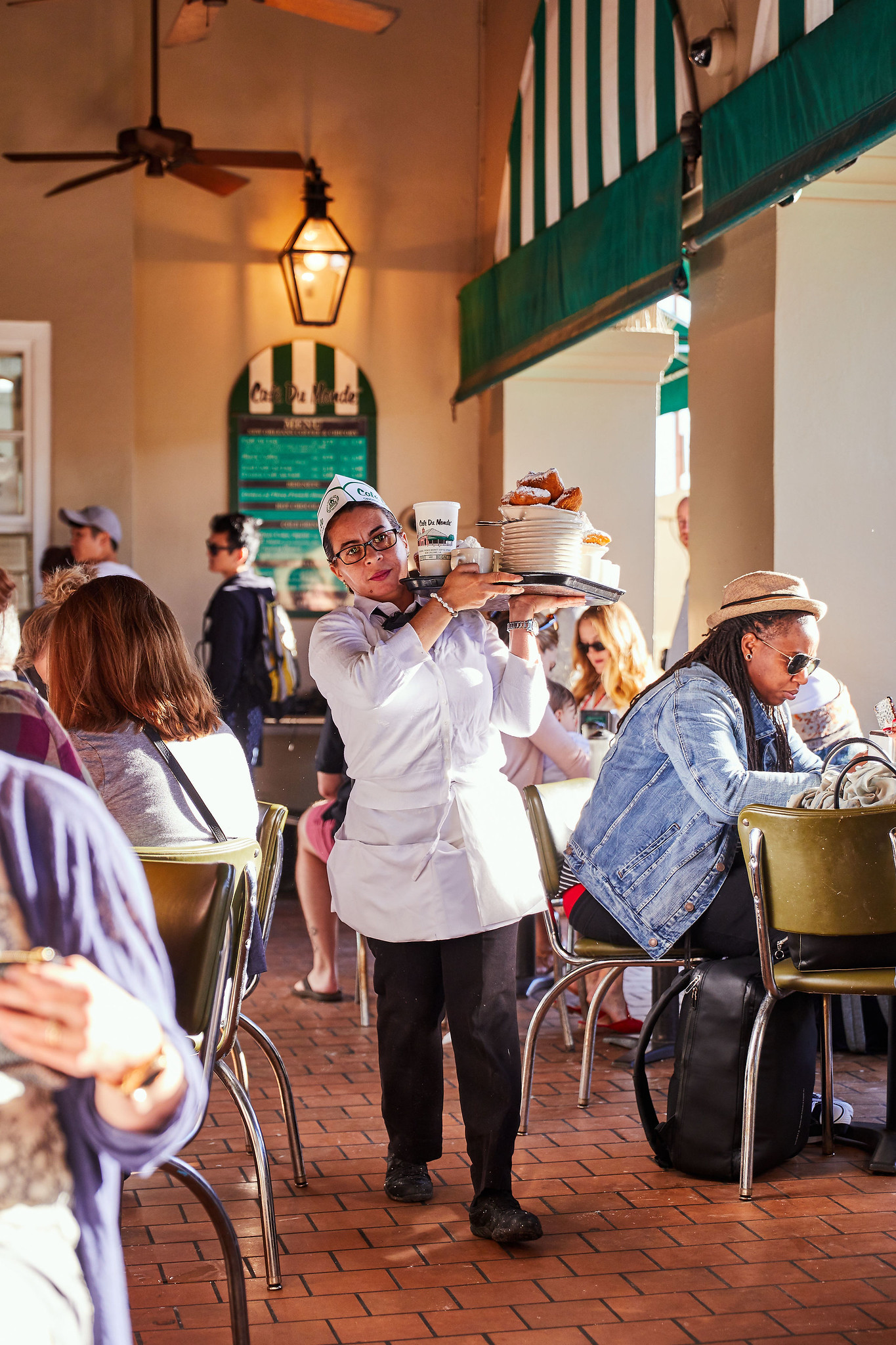 A server carries a tray of food through a busy restaurant patio.
