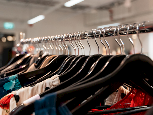 Clothes on hangers in a store, assorted colorful outfits on a rack, tight shot with blurred background shelves and bright ceiling lights.