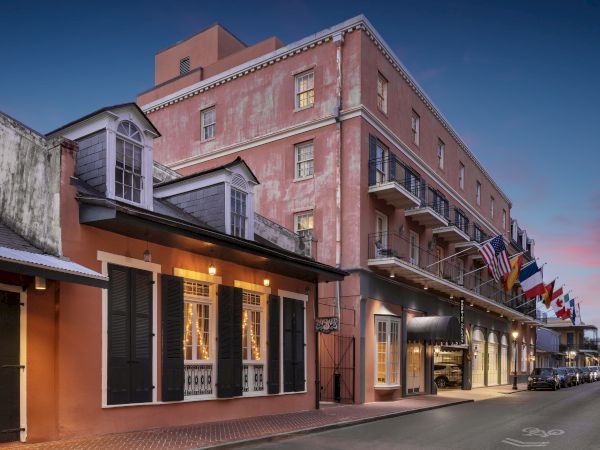 Historic brick street with pastel storefronts, balconies, and flags along a quiet evening avenue, charming colonial vibe and warm lights.