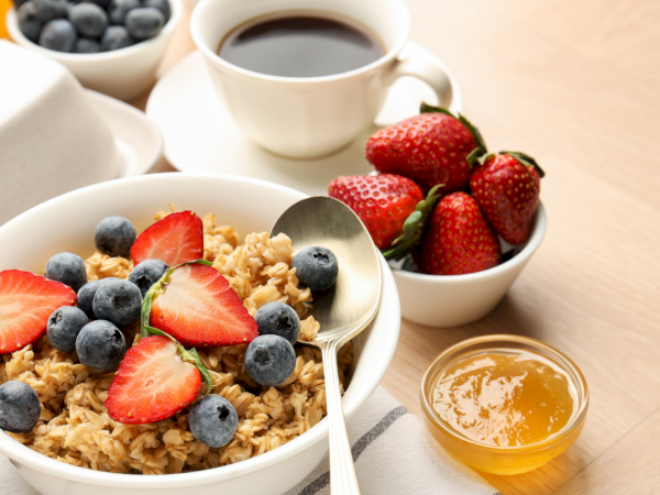 A breakfast setting with bowls of granola topped with strawberries and blueberries, plus sides of coffee, honey, and fresh fruit.