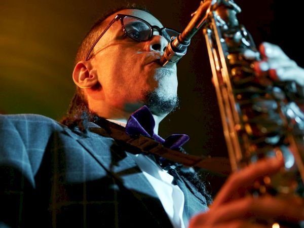 A saxophonist in a suit and sunglasses playing on stage, close-up with dramatic lighting, intense performance vibes.