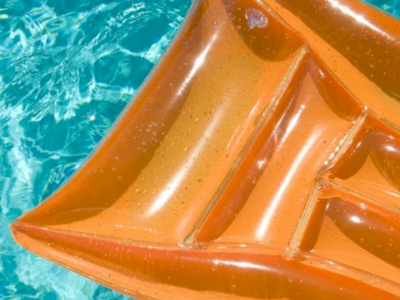 Orange inflatable river raft on clear blue water, close-up of its glossy folds and sunlight reflections.