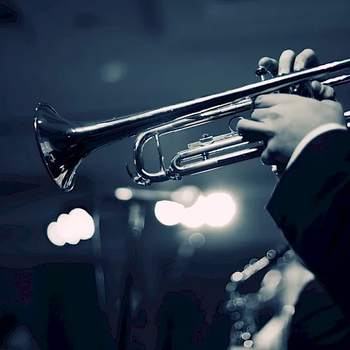 A musician plays a silver trumpet onstage under blue concert lights.