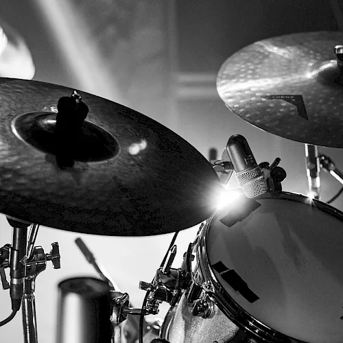 A black-and-white close-up of a drum set with cymbals, toms, and a microphone recording the beat.